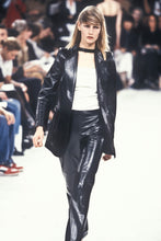 Load image into Gallery viewer, A model walks the runway wearing a glossy black leather blazer and matching pants over a white top, with a blurred audience in the background. From Ann Demeulemeester runway 1997 collection . 
